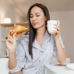 woman in robe enjoying croissant and coffee