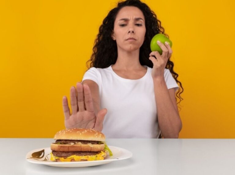 A woman in a white shirt holds a burger with a thoughtful expression. She's against a bright yellow background, creating a vibrant, lively atmosphere.