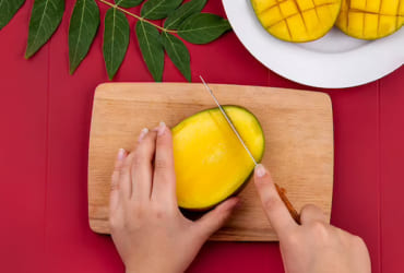 Hand peeling yellow mango on wood board