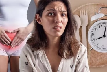 A woman with long dark hair and a cheerful expression sits outdoors. She wears a light patterned blouse. Background is blurred, suggesting a sunny day.